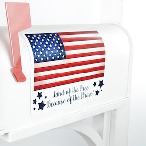 May include: White mailbox with an American flag design. The flag is red, white, and blue, with the text "Land of the Free Because of the Brave" and "Custom". The mailbox has a red flag and is mounted on a white post.