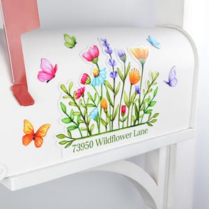 May include: White mailbox decorated with colorful watercolor flowers and butterflies. The mailbox has a red flag and the text "73950 Wildflower Lane" is printed on the side.