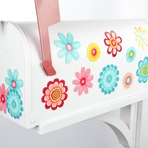 May include: White mailbox with colorful flower decals. The mailbox has a red flag and a white stand.