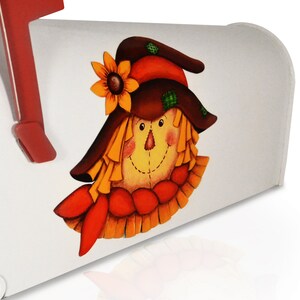 May include: A white mailbox with a painted scarecrow face. The scarecrow has a brown hat with a yellow sunflower, a red and orange scarf, and a yellow straw-like face.