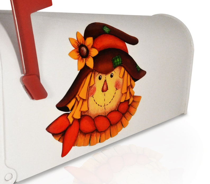 May include: A white mailbox with a painted scarecrow face. The scarecrow has a brown hat with a yellow sunflower, a red and orange scarf, and a yellow straw-like face.