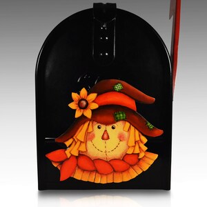 May include: Black metal mailbox with a painted scarecrow face. The scarecrow has a brown hat, orange and green accents, and a yellow beard.