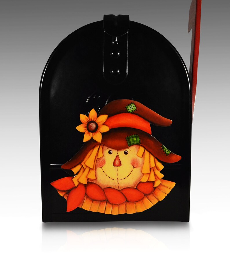 May include: Black metal mailbox with a painted scarecrow face. The scarecrow has a brown hat, orange and green accents, and a yellow beard.