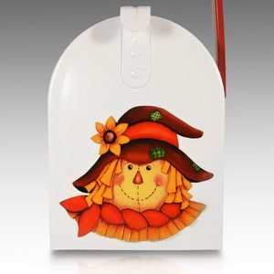May include: White metal mailbox with a painted scarecrow design. The scarecrow has a brown hat, orange hair, a yellow face, and a red scarf.