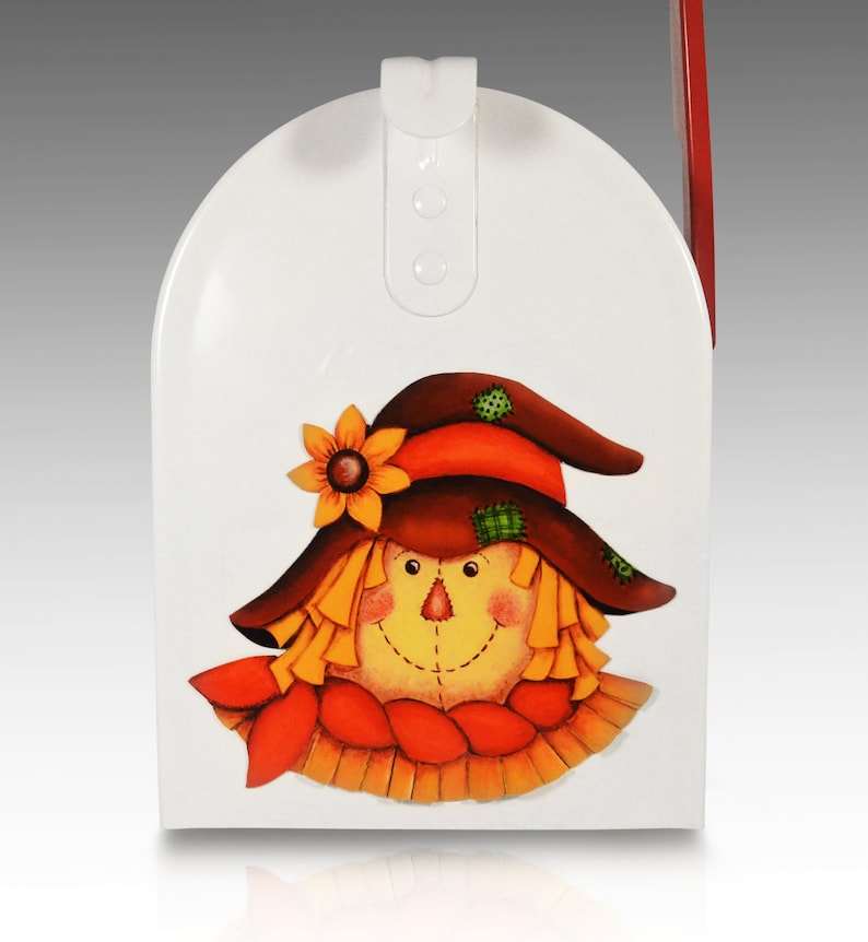 May include: White metal mailbox with a painted scarecrow design. The scarecrow has a brown hat, orange hair, a yellow face, and a red scarf.