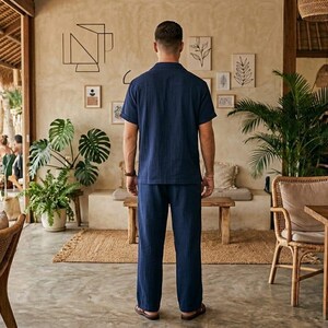 May include: A person wearing a navy blue short-sleeved shirt and matching pants. The outfit is a casual style, suitable for warm weather. The person is standing in a cafe or restaurant setting, with natural light and decor.