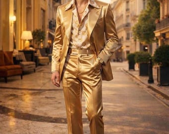 May include: A gold satin suit, including a blazer and flared trousers, worn over a patterned button-down shirt. The suit is a shiny, solid color. The person is wearing a gold chain and a watch. The background shows a European street.