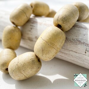 May include: A strand of light beige, cylindrical wooden beads with a textured, matte finish and visible natural grain lines. Each bead features a central hole for stringing. The logo CEYLON WOODEN CRAFT is visible in the bottom right corner.