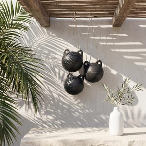 May include: Three matte black spherical hanging planters suspended by thin cords. Each planter features two small circular handles at the top. The planters are arranged in a cluster, showcasing a smooth, dark finish against a light-coloured wall.