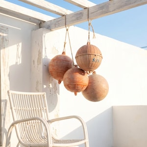 May include: A cluster of four spherical, weathered terracotta-coloured nautical buoys suspended by thick rope from a wooden beam. The buoys feature a textured, ribbed surface with visible signs of wear and a small blue marking on one sphere.