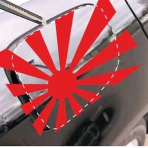 Op de afbeelding: Een rood en witte afbeelding van de Japanse Vlag van de Rijzende Zon aangebracht op een zwarte auto. Het ontwerp is een cirkel met rode stralen die uit het midden komen, en is aangebracht op de brandstofklep van de auto.