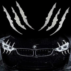Könnte beinhalten: Ein schwarzes Auto mit silbernen Krallenmarken-Aufklebern auf der Motorhaube und um die Scheinwerfer. Das Auto hat ein BMW-Emblem auf der Vorderseite.