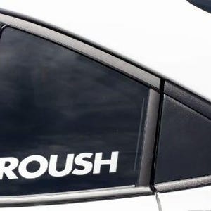 Puede incluir: Primer plano de una ventanilla de coche con la palabra "ROUSH" en letras blancas y en negrita. La ventanilla está oscurecida y la carrocería del coche es blanca. El marco de la ventanilla es negro.