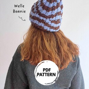 May include: A crochet beanie featuring alternating horizontal stripes of light blue and dark brown yarn. The text Welle Beanie is printed to the left of the hat, and a circular white graphic with the text PDF PATTERN is centered below.