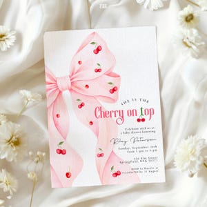 Puede incluir: Una invitación a un baby shower con un diseño de acuarela. La invitación presenta un lazo rosa adornado con cerezas rojas. El texto dice "She is the Cherry on top" e incluye detalles del evento: fecha, hora, lugar e información de RSVP.