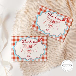 Two matching Baby-Q thank you cards on cream textured fabric with white ribbon. Red gingham background with blue scalloped border frames clothesline with baby items and BBQ grill illustration. Text reads "Thank you" and "with love, Olivia" in red script. Editable Canva template shown with decorative stars and utensils.