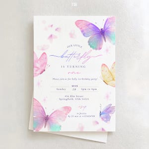 May include: A white invitation card featuring watercolour butterflies in shades of pink, purple, and yellow. The text reads "Our Little Butterfly is Turning One" with party details: date, time, and location.