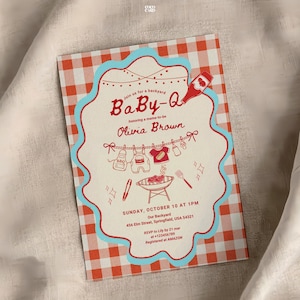 Baby-Q shower invitation on white fabric with red gingham border and turquoise scalloped frame. Features clothesline with baby items (sauce bottle, onesie, bib, bottle) and charcoal grill with spatula. Honors Olivia Brown, Sunday October 10 at 1PM, 456 Elm Street Springfield. RSVP to Lily by March 21. Registered at Amazon.