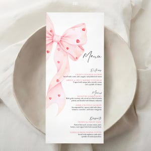 Könnte beinhalten: Eine Menükarte mit einem rosa Aquarell-Schleife und Herz-Akzenten. Die Speisekarte listet Vorspeisen, Hauptgerichte und Desserts auf. Die Karte befindet sich auf weißem Hintergrund und in einer weißen Schüssel.
