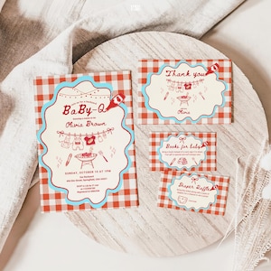 Baby-Q shower invitation suite on white wooden board over linen fabric. Red gingham cards with turquoise scalloped borders include main invitation for Olivia Brown (Sunday October 10, 1PM, 456 Elm Street Springfield), thank you card, books for baby request, and diaper raffle card. Features clothesline with baby items and BBQ grill illustrations.