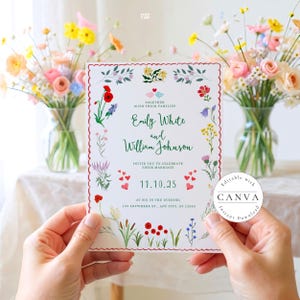 A beautiful wedding invitation held by hands against a floral background. The invitation features a delicate floral border with colorful wildflowers and small hearts. It reads: "TOGETHER WITH THEIR FAMILIES, Emily White and William Johnson INVITE YOU TO CELEBRATE THEIR MARRIAGE on 11.10.25 at six in the evening, 123 ANYWHERE ST., ANY CITY, ST 12345." The card has a scalloped red border and green calligraphy. Two glass vases with colorful flowers create a soft, romantic atmosphere.