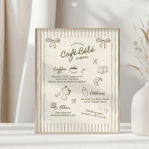 以下が含まれることがあります： ベージュと白のストライプの背景を持つ「Café Bébé」の額入りメニュー。メニューには、コーヒー、追加オプション、その他のドリンクオプションがあり、コーヒーカップ、クロワッサン、哺乳瓶のイラストが描かれています。