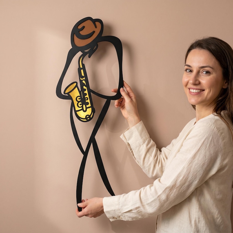 May include: A black metal wall art piece depicting a stylized figure wearing a brown hat and playing a gold saxophone. The design features clean, continuous lines forming the silhouette of a musician, with the instrument highlighted in yellow.