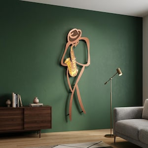 May include: A wall-mounted metal sculpture depicting a stylized figure wearing a hat and playing a gold-colored saxophone. The outline of the figure is rendered in a copper-toned finish, creating a minimalist silhouette against the wall surface.