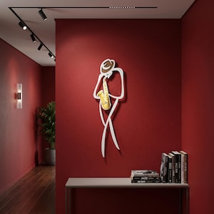 May include: A wall-mounted metal art piece depicting a stylized figure wearing a hat and playing a yellow saxophone. The sculpture features clean, white outlines forming the silhouette of a musician, with a distinct yellow instrument accent.