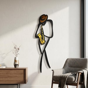 May include: A wall-mounted metal art piece depicting a stylized black silhouette of a person wearing a brown hat and playing a bright yellow saxophone. The design features clean, minimalist lines that form the figure of a musician in motion.
