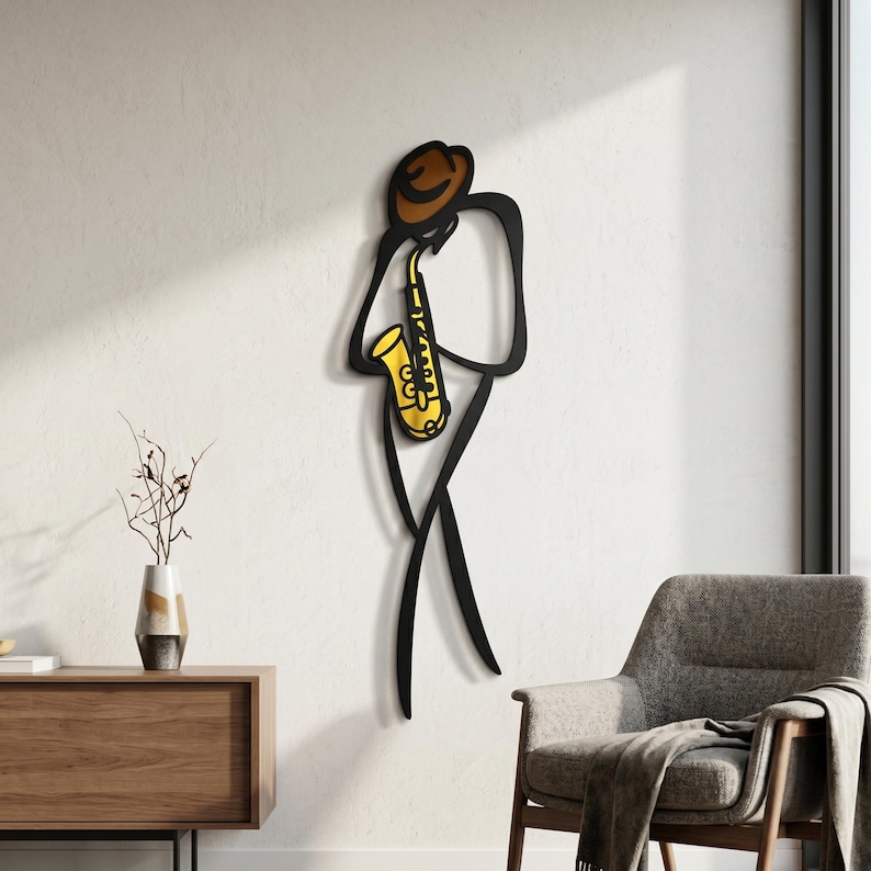May include: A wall-mounted metal art piece depicting a stylized black silhouette of a person wearing a brown hat and playing a bright yellow saxophone. The design features clean, minimalist lines that form the figure of a musician in motion.