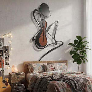 May include: A metal wall art piece depicting a woman with a guitar. The artwork is black with a brown guitar body. The bedroom features a bed with a patterned quilt, a guitar, and a small side table with a lamp.
