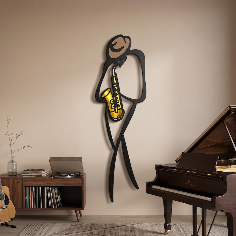 May include: A wall-mounted metal art piece depicting a stylized figure wearing a hat and playing a gold-colored saxophone. The figure is outlined in black, with a tan-colored hat and a bright gold saxophone, creating a minimalist musical silhouette.