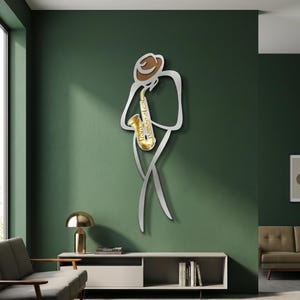 May include: A wall-mounted metal art piece depicting a stylized figure wearing a brown hat and playing a gold saxophone. The figure is outlined in a silver metallic finish, creating a minimalist silhouette that stands out against the wall surface.