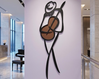Op de afbeelding: Een metalen wanddecoratie die een gestileerde figuur voorstelt die cello speelt. De figuur is weergegeven in zwarte lijnen met een bruine, ovaalvormige celloklankkast. Het ontwerp toont het silhouet van een muzikant die een hoed draagt.