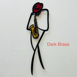 May include: A black metal wall art piece depicting a stylized figure wearing a red hat and playing a yellow saxophone. The design features clean, minimalist lines forming the silhouette of a musician. The text Dark Brass is printed in red.