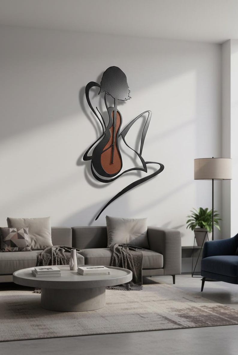 May include: A black metal wall art piece depicting a figure playing a guitar. The guitar has a brown body. The art is mounted on a white wall above a gray sofa and coffee table, creating a modern aesthetic.