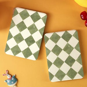 May include: Two rectangular coasters with a green and white checkered pattern are displayed on an orange surface. The coasters are next to a small bunny figurine, a blue ball, a lemon, and cherries. The coasters are a decorative item.