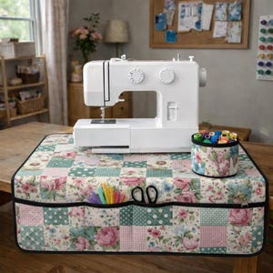 May include: A white sewing machine rests on a floral patchwork cover. The cover features pockets with scissors and pencils. A matching container holds thread spools. The cover is on a wooden table.