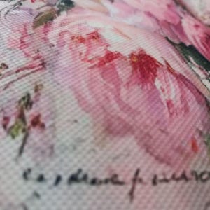 May include: A textured fabric surface featuring a soft watercolor-style print of pink and white roses with green leaves. The design includes faint, dark cursive script layered over the floral pattern, creating a layered visual effect on the material.