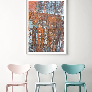May include: Three chairs with heart-shaped backs in a room with a framed abstract painting of rusty metal. The chairs are pink, light blue, and teal.