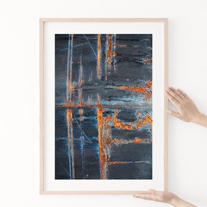 May include: Abstract art print in a wooden frame. The print features a dark blue and orange color scheme with a rusty, textured surface.