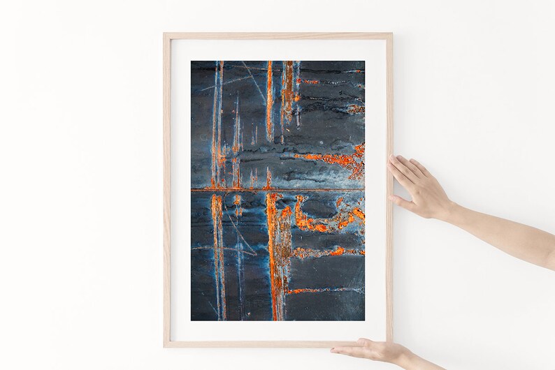 May include: Abstract art print in a wooden frame. The print features a dark blue and orange color scheme with a rusty, textured surface.