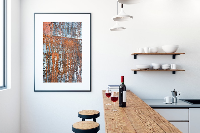 May include: A rustic wooden countertop with two bar stools, two glasses of red wine, and a bottle of wine. The countertop is in front of a white wall with a framed abstract painting and two wooden shelves with white dishes.