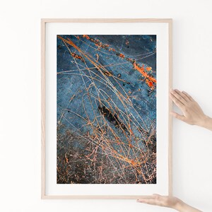 May include: Abstract art print with a blue background and orange and white lines. The print is framed in a light wood frame.