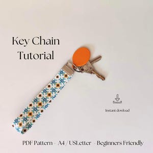 Pode incluir: Um tutorial de chaveiro com uma alça estampada com desenhos florais azuis, amarelos e brancos. O texto "Key Chain Tutorial" é exibido acima do chaveiro. A imagem também inclui chaves e uma etiqueta laranja.