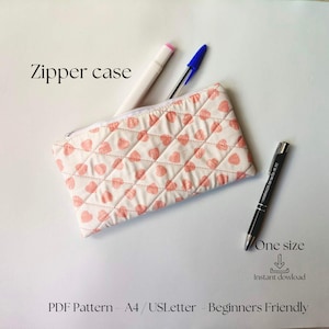 Pode incluir: Um estojo com zíper acolchoado com um padrão de corações rosa, acompanhado por um marcador branco e rosa, uma caneta azul e uma caneta preta. O texto "Zipper case" está acima do estojo. Os textos "One size" e "Instant download" também são visíveis.