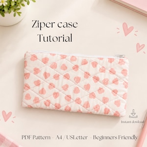 Pode incluir: Um estojo retangular acolchoado com fecho, em tecido branco com um padrão repetitivo de pequenos corações cor-de-rosa. O texto "Ziper case Tutorial", "Instant dowload" e "PDF Pattern - A4/USLetter - Beginners Friendly" é visível.