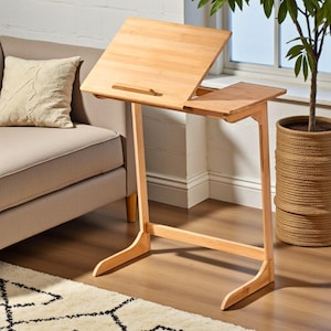 May include: A light-coloured bamboo laptop desk with an adjustable angled top and a small side table. The desk has a simple, minimalist design with a natural wood finish. The desk is 76 cm tall.