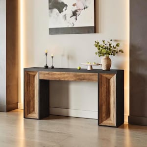 May include: A modern console table with a black top and geometric wooden accents. The table features a natural wood drawer front and side panels with a dark finish. Decorative items include candles, a vase with greenery, and a small fruit plate.